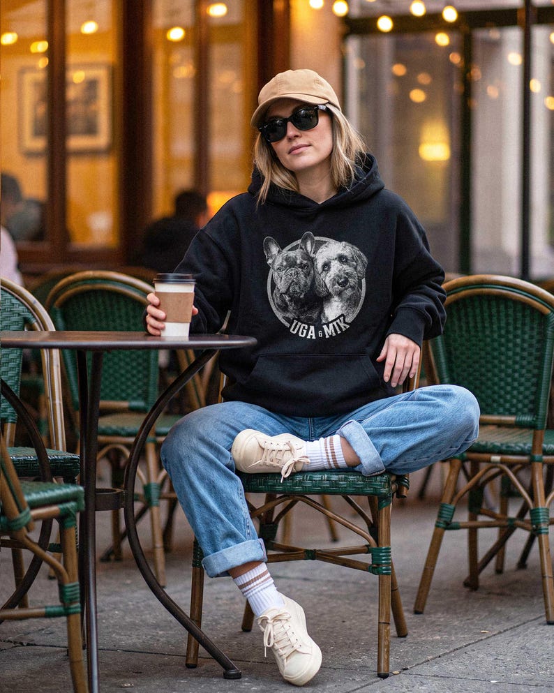 Puede incluir: Una sudadera negra con capucha que presenta un gr&aacute;fico circular de un Bulldog Franc&eacute;s y un perro tipo Doodle con el texto UGA & MIK impreso debajo. La sudadera tiene mangas largas, un bolsillo tipo canguro y se usa con pantalones vaqueros.