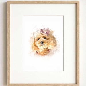 May include: A framed watercolor print featuring a portrait of a light brown curly-haired dog with a small bow on its head. The artwork is set within a light-colored wooden frame with a white mat, showcasing soft paint splatters and brush strokes.