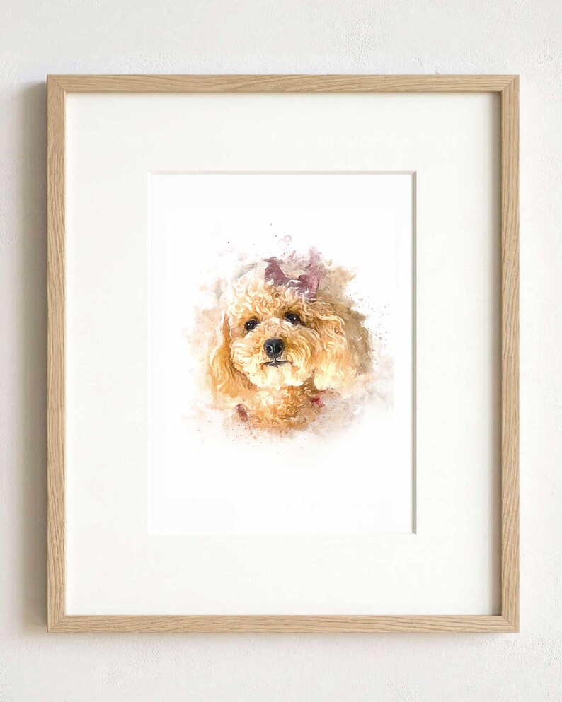 May include: A framed watercolor print featuring a portrait of a light brown curly-haired dog with a small bow on its head. The artwork is set within a light-colored wooden frame with a white mat, showcasing soft paint splatters and brush strokes.