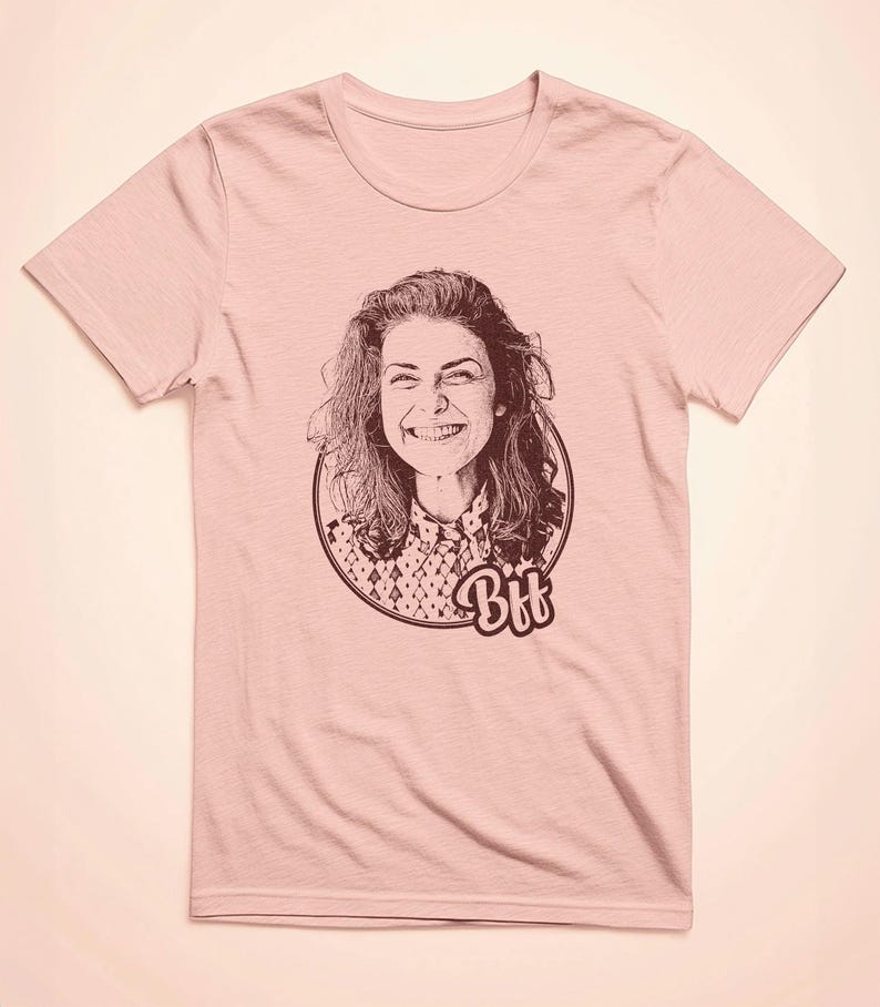 May include: A pink t-shirt featuring a black and white illustration of a woman smiling. The illustration is within a circle with the word "Bff" underneath.