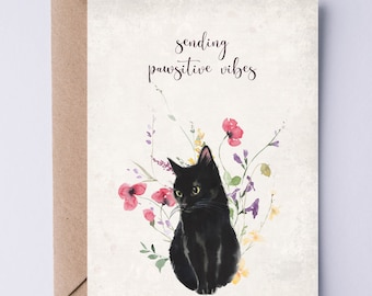 Könnte beinhalten: Eine Grußkarte mit einer schwarzen Katze, die in einem Blumenfeld sitzt. Der Text auf der Karte lautet "sending pawsitive vibes".