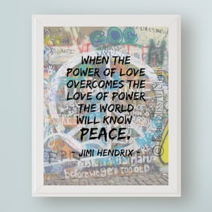 Op de afbeelding: Een ingelijst print met een kleurrijke graffiti-achtergrond met een vredesteken en een citaat van Jimi Hendrix: "Wanneer de kracht van liefde de liefde voor macht overwint, zal de wereld vrede kennen."