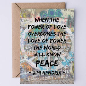 Op de afbeelding: Een kleurrijk vredesteken met graffiti op een muur, met de quote "Wanneer de kracht van liefde de liefde voor macht overwint, zal de wereld vrede kennen - Jimi Hendrix".