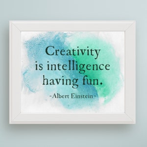 May include: A white framed print with a blue and green watercolour background. The quote "Creativity is intelligence having fun." is printed in black text. The quote is attributed to Albert Einstein.