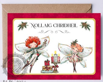 Può includere: Un biglietto di Natale con bordo rosso e interno bianco. Presenta due illustrazioni di fate e il testo "NOLLAIG CHRIDHEIL". Il biglietto è accompagnato da una busta marrone.