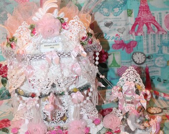 Puede incluir: Un árbol de Navidad decorativo y ornamentado, blanco y rosa, con encaje, perlas y detalles florales. El árbol está adornado con lazos rosas y un letrero que dice "CANDIES". La base está decorada con rosas rosas y un letrero que dice "ESTABLISHED 1936".