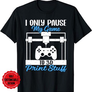 May include: Black t-shirt with a white and blue graphic. The graphic shows a 3D printer design with a game controller and the text "I ONLY PAUSE My Game TO 3D Print Stuff". A red circular sticker with the text "100% CUSTOMIZABLE DESIGN" is in the lower left corner.