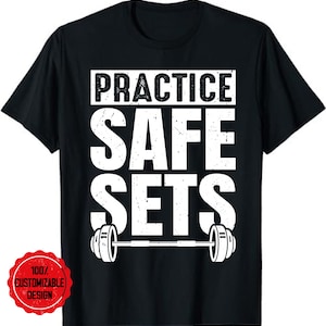 Könnte beinhalten: Schwarzes T-Shirt mit weißem Text, der "Practice Safe Sets" lautet, mit einer Langhantel und Gewichten darunter.