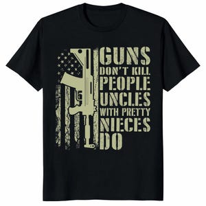 Könnte beinhalten: Schwarzes T-Shirt mit einem verblassten amerikanischen Flaggen-Design und einem Gewehr. Der Text lautet "GUNS DON'T KILL PEOPLE UNCLES WITH PRETTY NIECES DO" in einer verblassten Schriftart.
