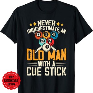 Może przedstawiać: Czarny T-shirt z grafiką w stylu vintage przedstawiającą kule bilardowe i kije bilardowe. Tekst brzmi: "Nigdy nie lekceważ starego człowieka z kijem bilardowym."