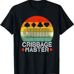 May include: A black t-shirt with a vintage-style design featuring a cribbage board and playing cards. The text "Cribbage Master" is printed below the design.