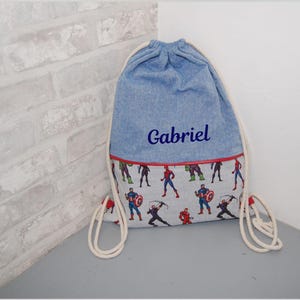 Peut inclure: Sac à cordon en jean bleu avec le nom "Gabriel" brodé en bleu. La partie inférieure présente un motif de super-héros. Le sac a des cordons de serrage en corde blanche et une bordure rouge.