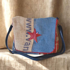Peut inclure: Sac à bandoulière rectangulaire avec un design patchwork. Il présente un devant bleu denim, un côté en toile de jute avec le texte "www.van" et une étoile rouge. Il a une sangle bleue et une bordure rouge.
