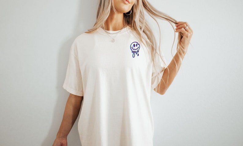 May include: A white t-shirt with a blue and purple dripping smiley face graphic.