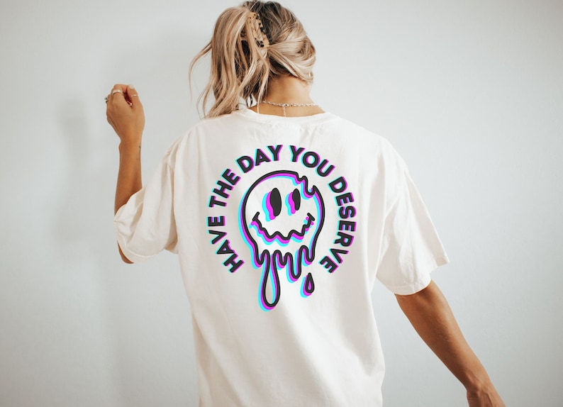 May include: White t-shirt with a black and blue graphic on the back. The graphic is a melting smiley face with the text "Have the day you deserve" around it.
