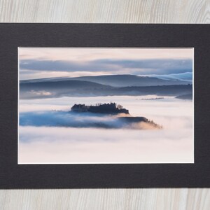May include: A black and white photograph of a castle on a hilltop, surrounded by fog. The castle is silhouetted against a cloudy sky.