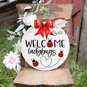 以下が含まれることがあります： 「WELCOME ladybugs」の文字が黒い筆記体で書かれた、丸い白い木製の看板。赤いテントウムシのイラストと赤いリボンが特徴です。造花と緑で飾られています。
