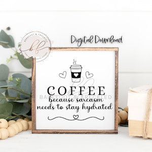 Può includere: Un cartello bianco con cornice in legno marrone, che presenta un'illustrazione in bianco e nero di una tazza di caffè con vapore che ne esce. Il testo sul cartello dice "COFFEE because sarcasm needs to stay hydrated".