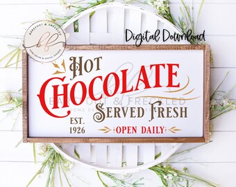 Könnte beinhalten: Ein rechteckiges Holzschild mit den Worten "Hot Chocolate Served Fresh" in roter und brauner Schrift. Das Schild enthält auch den Text "Est. 1926" und "Open Daily". Das Schild ist von weißen Blumen und Grün umgeben.