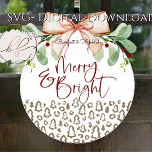 May include: A white round door hanger with a watercolor wreath of greenery and red berries. The wreath has a brown bow with a pink ribbon. The center of the hanger has the text "Merry & Bright" in red script font and a brown and white pattern of stylized trees.
