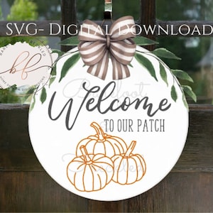 May include: A white round door hanger with a brown and white striped bow, green leaves, and the text "Welcome to our patch". Three orange pumpkins are drawn on the hanger.