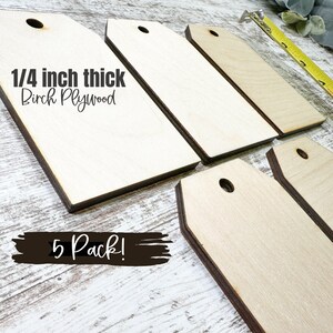 May include: Five unfinished wooden tags made of 1/4 inch thick birch plywood. Each tag has a hole at the top and a rounded edge. The tags are arranged in a staggered pattern on a light wood surface. The text "1/4 inch thick Birch Plywood" and "5 Pack!" is visible in the image.