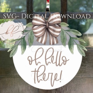 May include: A white round door hanger with the text "oh hello there!" in brown script. The hanger is decorated with a brown and white striped bow and green watercolour leaves.