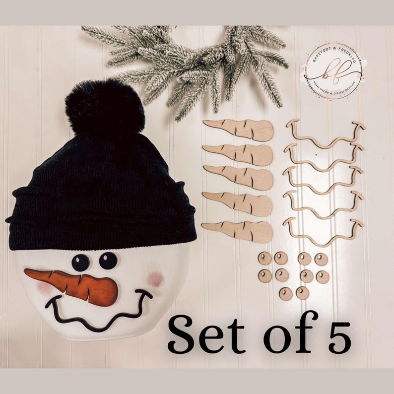 Op de afbeelding: Set van 5 houten sneeuwpop-knutselstukken. Bevat een zwarte hoed met een pompon, een wortelneus, twee ogen en een mond. De stukken zijn onbewerkt en klaar om te worden geschilderd of versierd.