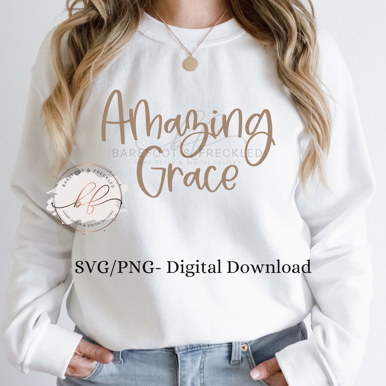 May include: A white sweatshirt with the text "Amazing Grace" in brown lettering. The text "BAREFOOT & FRECKLED" is also in brown lettering below the main text. The image includes a logo for the company.