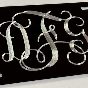May include: A black license plate with a silver monogram of the letters "DFS" in a cursive script.