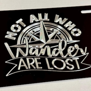 May include: Black metal license plate with a silver design featuring a compass and the text "Not all who wander are lost."