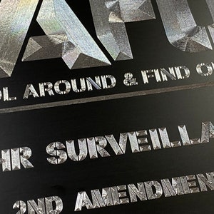 Pu&ograve; includere: Un cartello nero e argento con il testo "Don't Cool Around & Find Out" e "2nd Amendment" in un carattere geometrico audace.