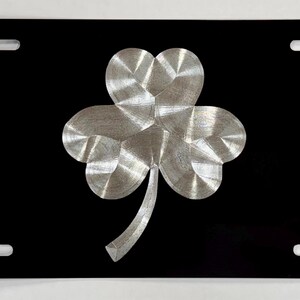 May include: Black metal license plate with a silver shamrock design.