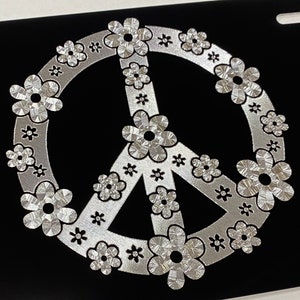 May include: A silver peace sign with a flower design on a black background.