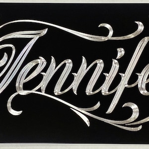 May include: A black license plate with the name "Jennifer" engraved in silver script.