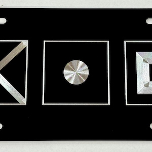 May include: Black license plate with three silver-colored squares. The first square has a silver X inside, the second square has a silver circle inside, and the third square has a silver square inside.