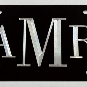 May include: Black license plate with silver lettering that reads "AMR".
