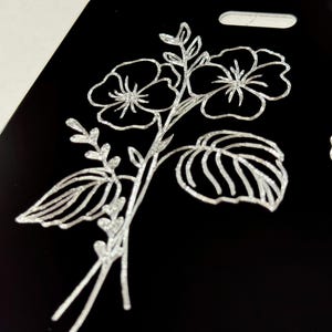 Peut inclure: Un motif floral argent&eacute; paillet&eacute; sur fond noir. Le motif repr&eacute;sente deux fleurs &agrave; cinq p&eacute;tales chacune, des feuilles et des tiges.