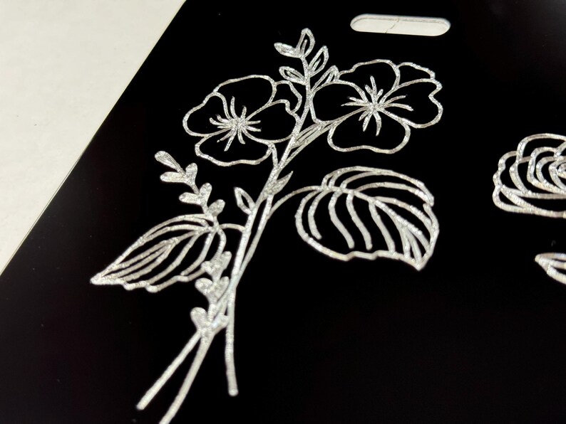 Peut inclure: Un motif floral argent&eacute; paillet&eacute; sur fond noir. Le motif repr&eacute;sente deux fleurs &agrave; cinq p&eacute;tales chacune, des feuilles et des tiges.