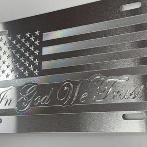 Può includere: Targa argentata con un disegno inciso della bandiera americana. La bandiera comprende stelle e strisce, con la frase "In God We Trust" in un carattere decorativo. La targa ha quattro fori di montaggio.