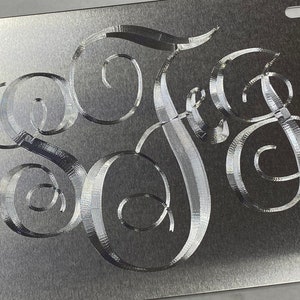 May include: A silver metal license plate with a monogram of the letters "SAG" in a decorative script font.