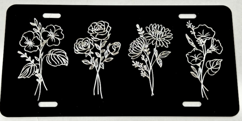 Peut inclure: Quatre motifs floraux diff&eacute;rents sont grav&eacute;s en blanc sur un fond noir. Les motifs comprennent un bouquet de roses, un bouquet de marguerites, un bouquet de belles-de-jour et un bouquet de pens&eacute;es.