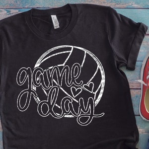 May include: Black t-shirt with a white volleyball graphic and the text "game day" in a distressed font. Two small hearts are above the word "day".