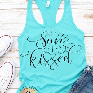 May include: A turquoise tank top with the text "Sun Kissed" in black script. The tank top is styled with denim shorts and white sneakers.