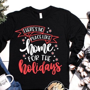May include: Black long-sleeve shirt with a red and white graphic that says "There's no place like home for the holidays".