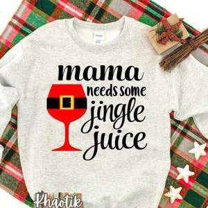 May include: Gray sweatshirt with the text "mama needs some jingle juice" and a red wine glass with a black belt around it. The text "Khaotik Kreations" is at the bottom of the sweatshirt.