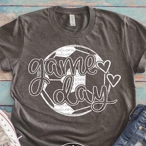 May include: A gray t-shirt with a white graphic of a soccer ball and the text "game day" with two hearts.