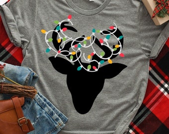 May include: A gray t-shirt with a black silhouette of a reindeer with colorful Christmas lights wrapped around its antlers. The text "Khaotik Kreations" is printed on the bottom of the shirt.