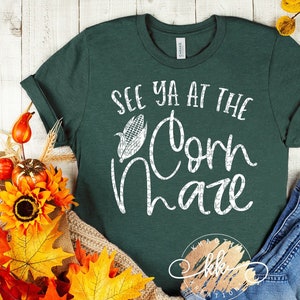 May include: A green t-shirt with the text "See ya at the Corn Maze" in white lettering. The shirt is decorated with a white corn cob graphic.