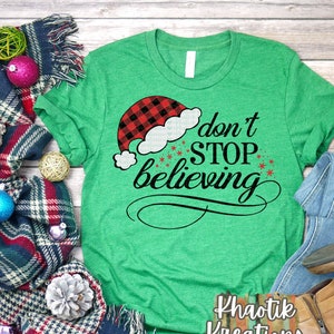 May include: Green t-shirt with a red and black buffalo plaid Santa hat graphic and the text "don't stop believing".